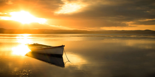 A peaceful and serene looking boat sits docked on the lake in the glowing afternoon sunlight.
